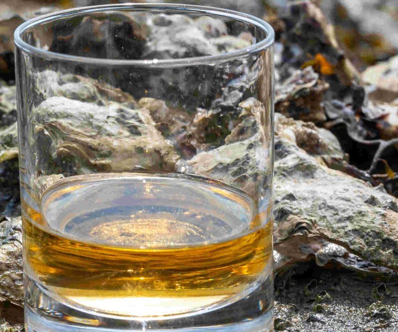 Two drams of whisky sitting on rocks by the water
