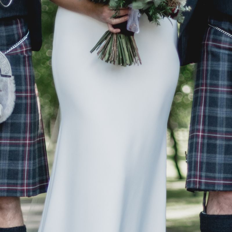 Scotsmen dressing in kilt on wedding day with bride in the middle.