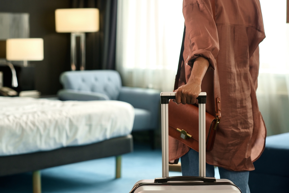 Close up of unrecognizable Black woman entering hotel room and holding suitcase upon travelling to resort copy space.