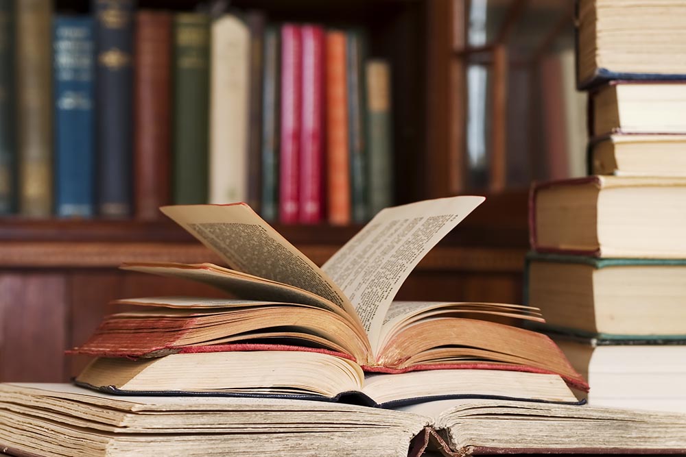 An open book on a table surrounded by other books.