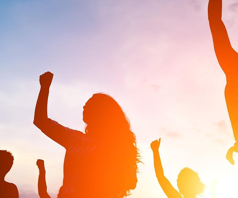 Festival goers dancing at sunset in silhouette.