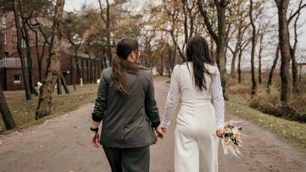 Backview of newlywed lesbian couple walking and holding each other hand on the road.