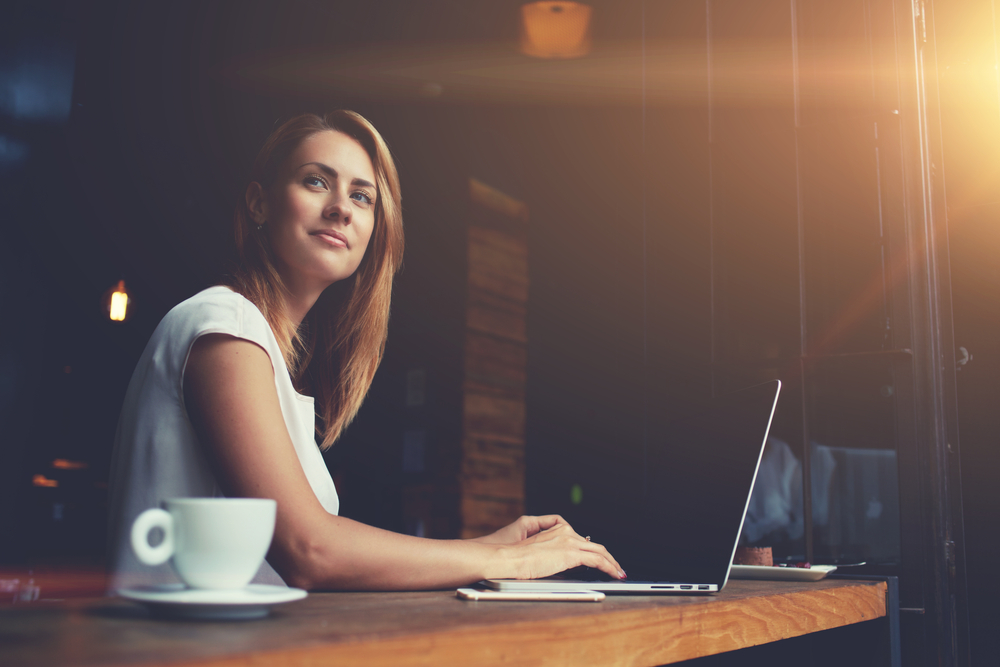 woman dreaming about something while sitting with portable net-book in modern cafe bar.
