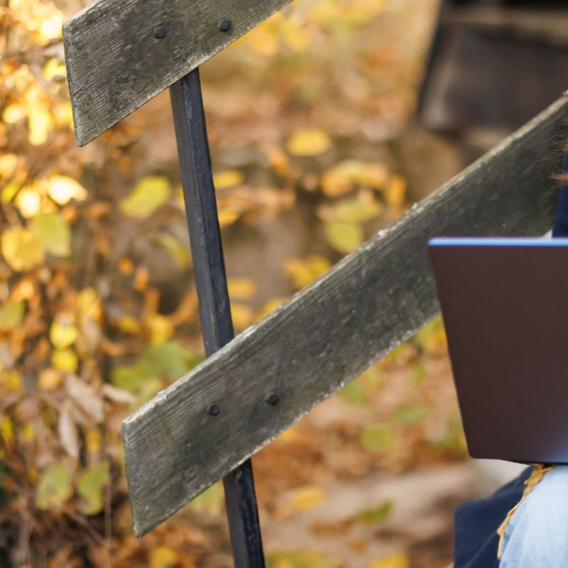 woman sitting on a step working on her laptop in autumn.
