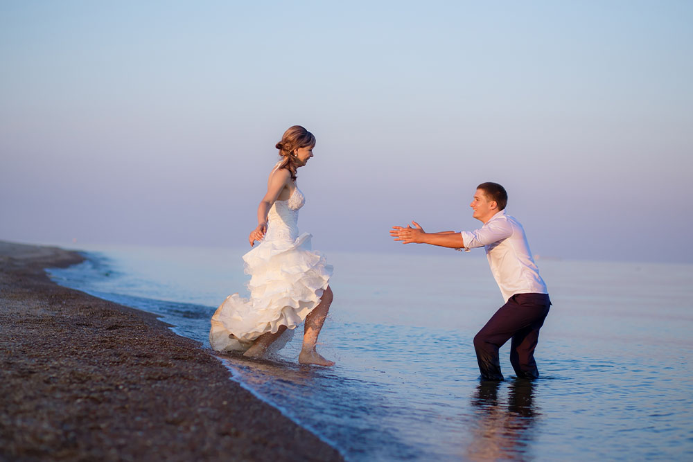 A bride and groom trashing a dress at the beach.